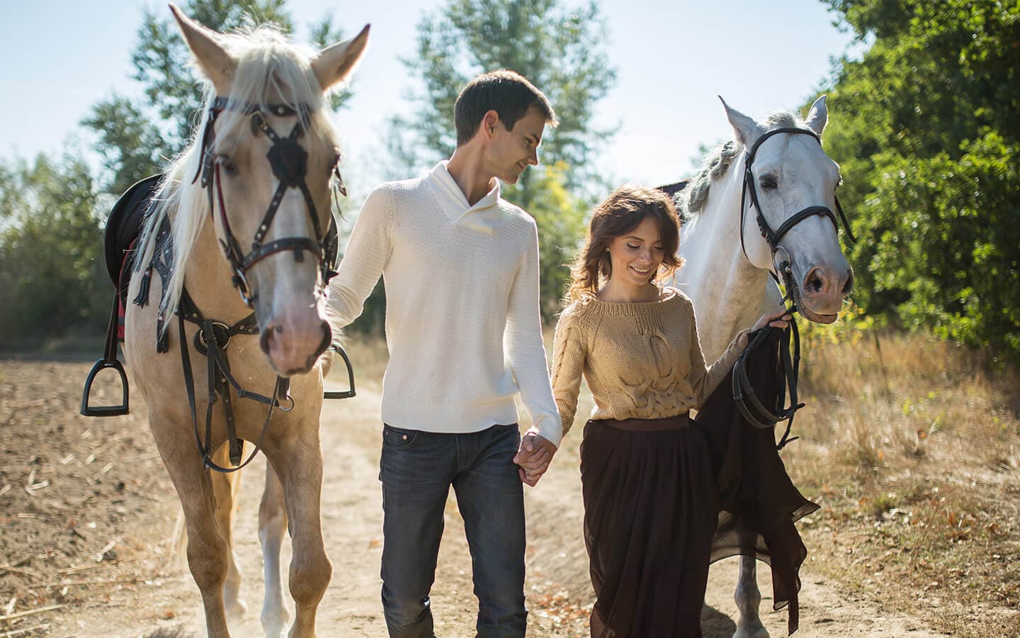 A couple walks hand in hand along a path, accompanied by two horses.