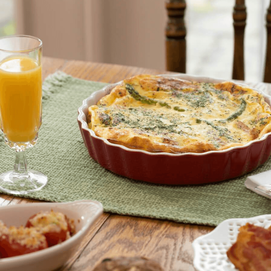 A savory baked dish with green vegetables sits on a table next to a glass of orange juice.