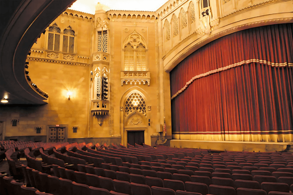 Interior of a grand theater featuring ornate architecture and a red stage curtain.