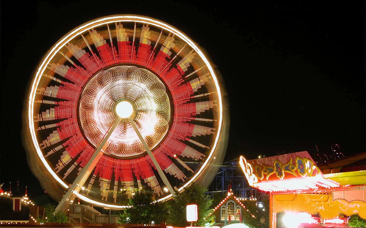A brightly lit Ferris wheel spins against a night sky.