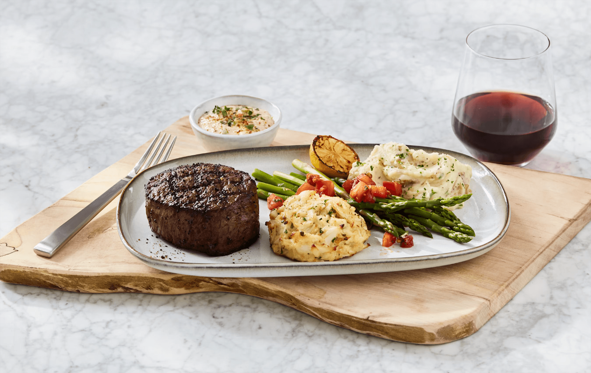 A gourmet meal featuring a grilled filet mignon, garlic mashed potatoes, asparagus, and a glass of red wine on a wooden board.