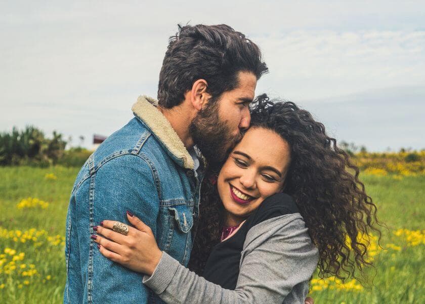 couple embracing and man kissing woman on forehead in spring meadow with yellow wildflowers couple embracing and man kissing woman on forehead in spring meadow with yellow wildflowers