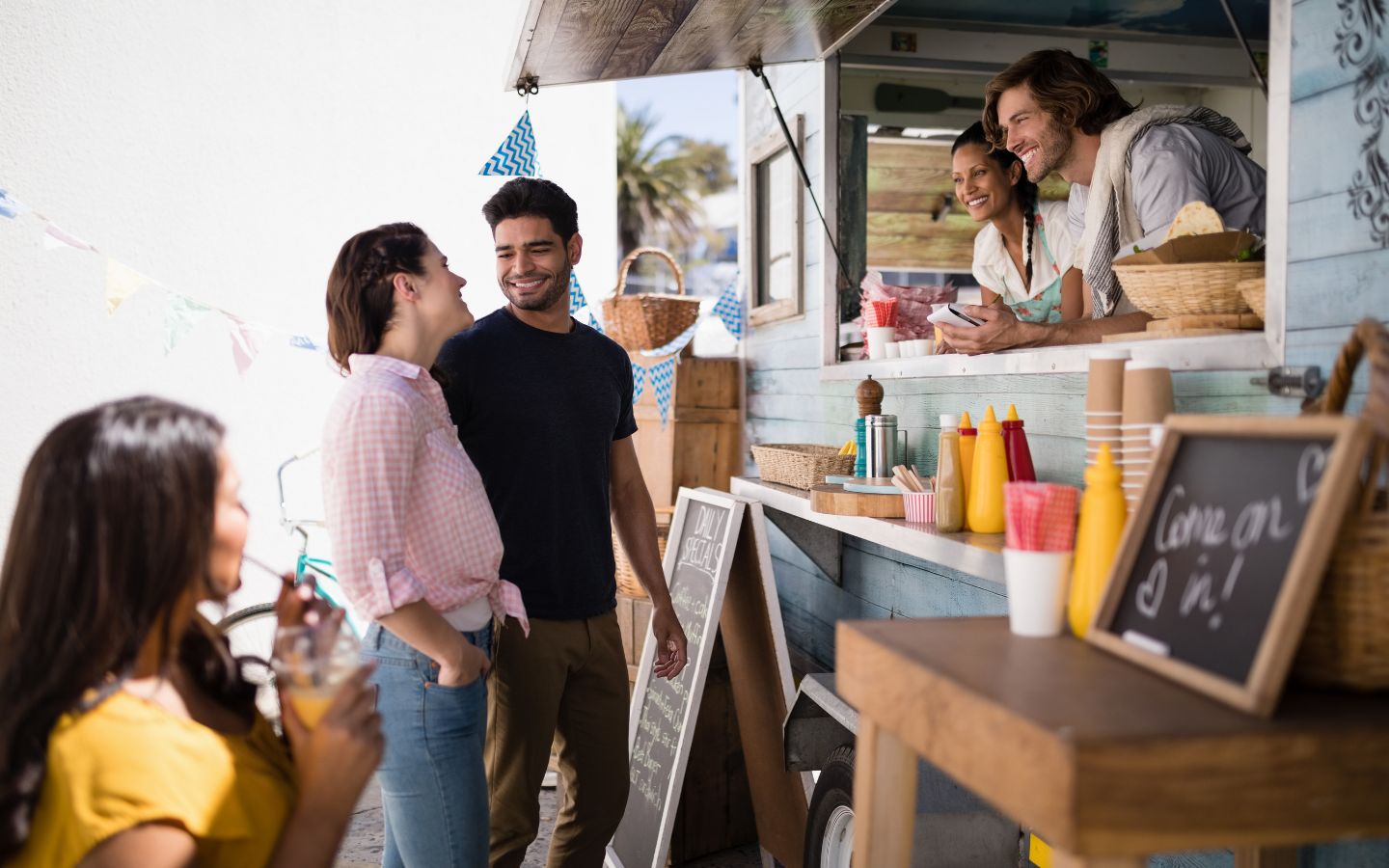 man and woman looking at each other about to place an order with another man and woman running a food truck while a woman waits in line nearby